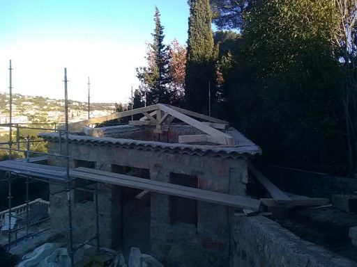 Charpente traditionnelle en bois à quatre pans en cours de réalisation sur une maison entourée d’un échafaudage.