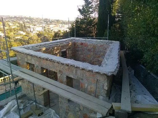 Vue plongeante sur une maison sans charpente, entourée d’un échafaudage.