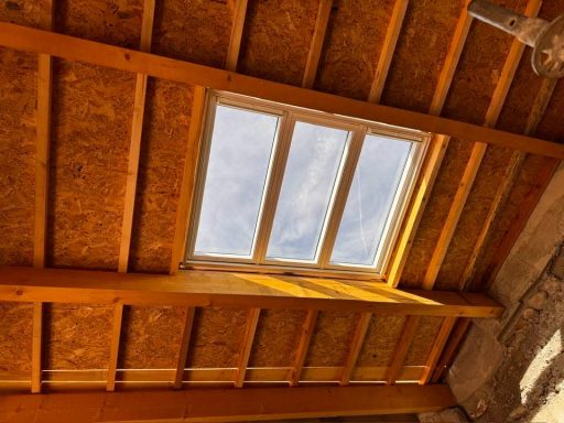 Charpente traditionnelle en bois vue de l’intérieur avec un Velux installé en toiture.